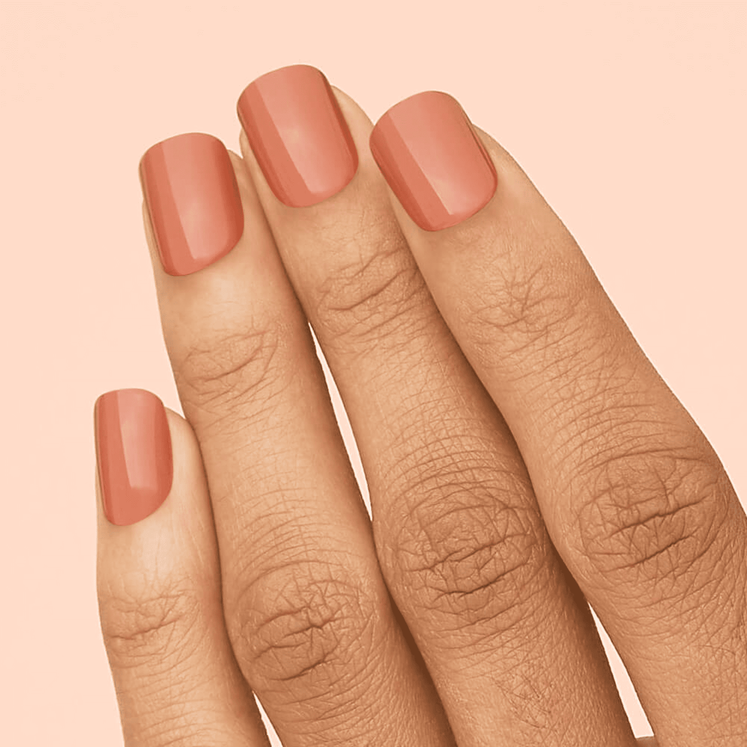 Fingertips with smooth, glossy press-on nails in a warm caramel shade against a soft peach background.