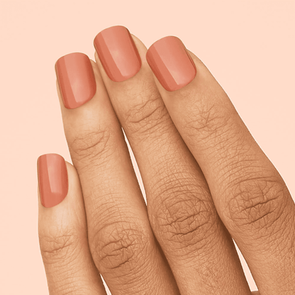 Fingertips with smooth, glossy press-on nails in a warm caramel shade against a soft peach background.