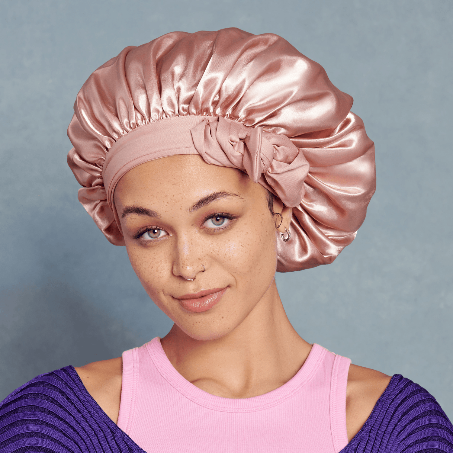 Woman wearing a pink satin bonnet against a gray background