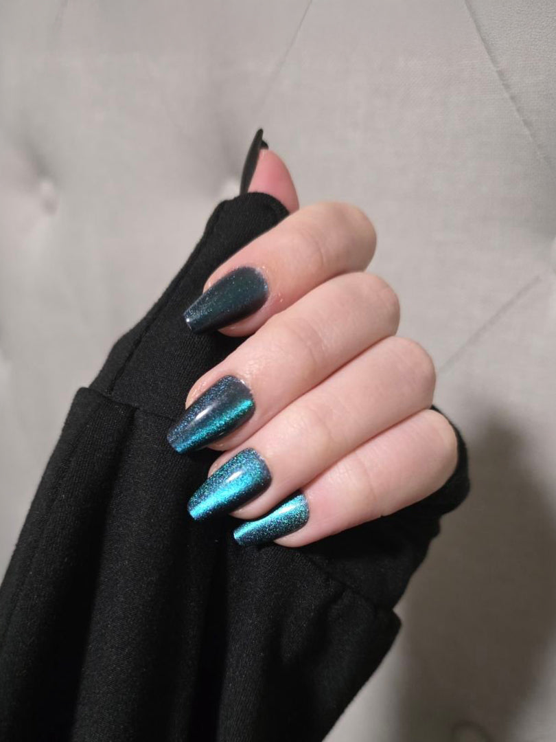 Hand with turquoise glitter coffin nails against black fabric background.