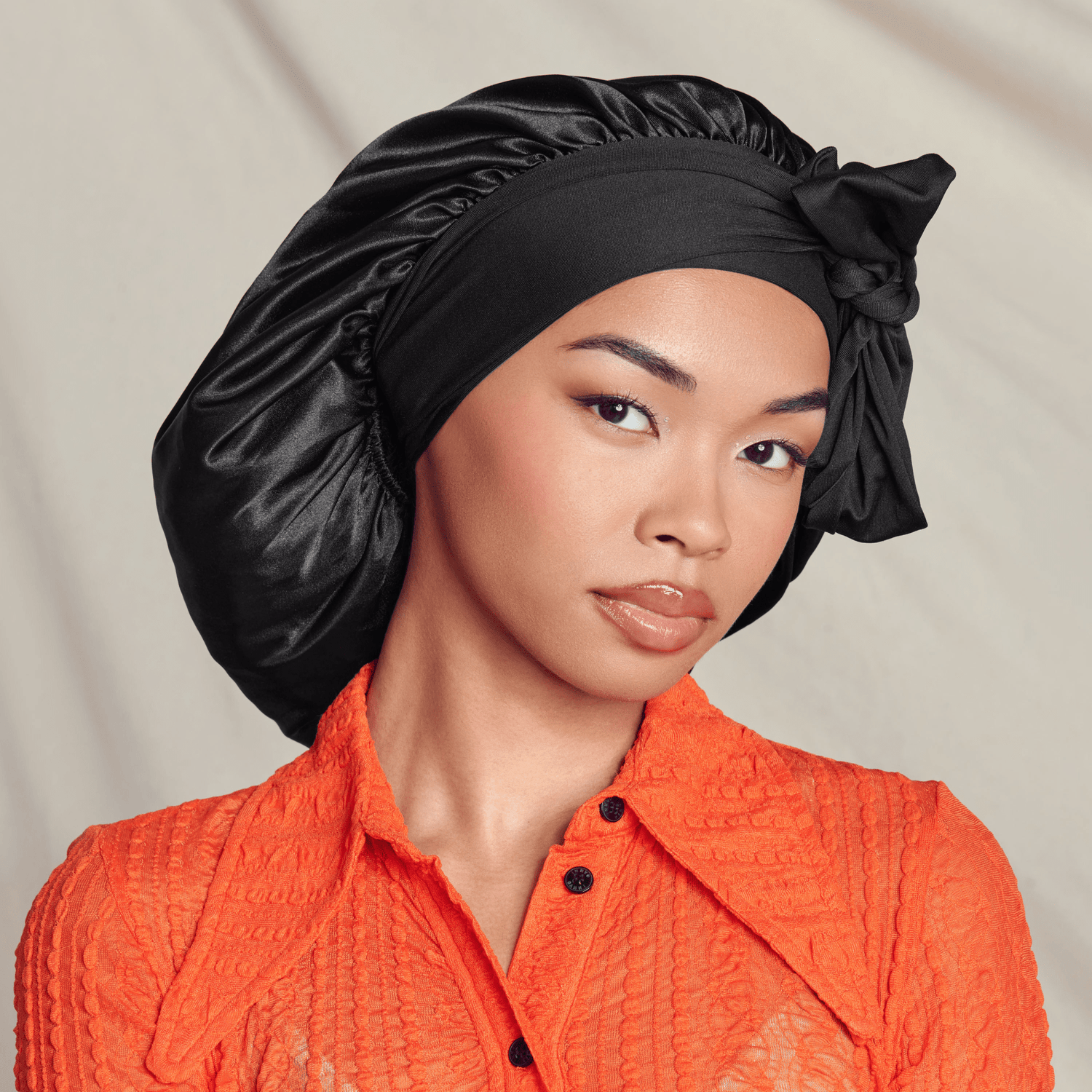 Woman wearing black silk bonnet and orange textured shirt, neutral background.