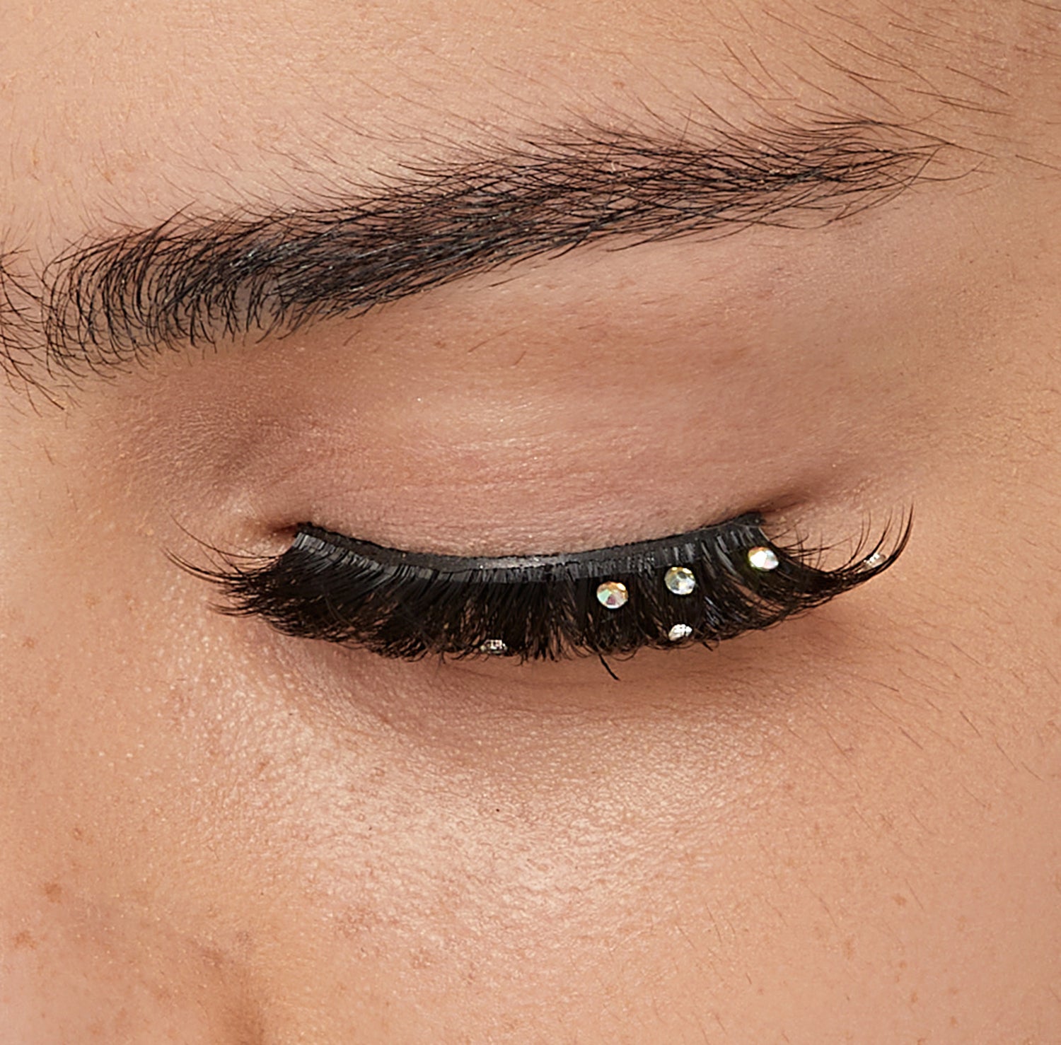 Closed eye with black volumized false lashes and iridescent rhinestone embellishments.