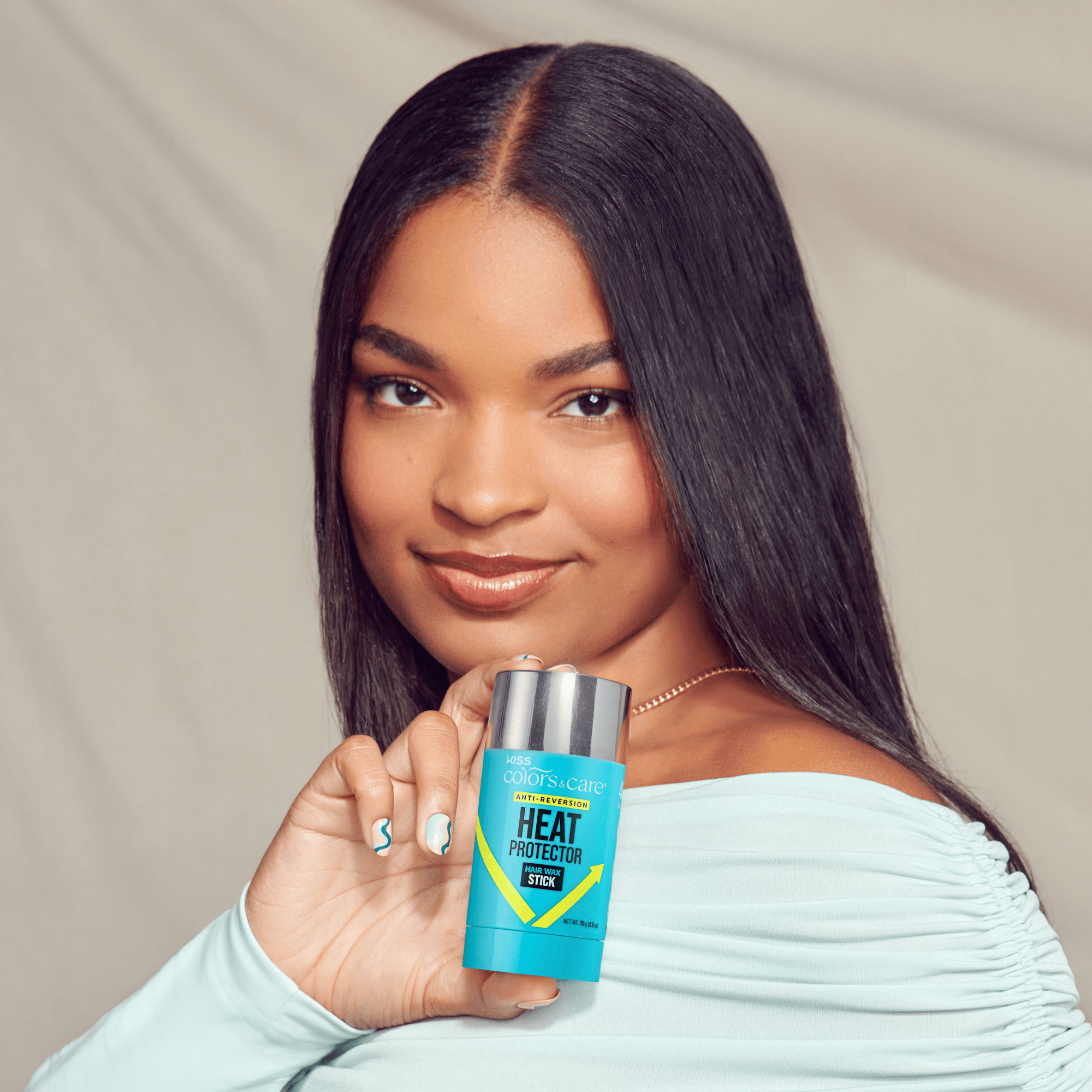 Woman with straight dark hair wearing a light blue top holds a blue KISS Colors &amp; Care Heat Protector Hair Wax Stick labeled "Anti-Reversion."