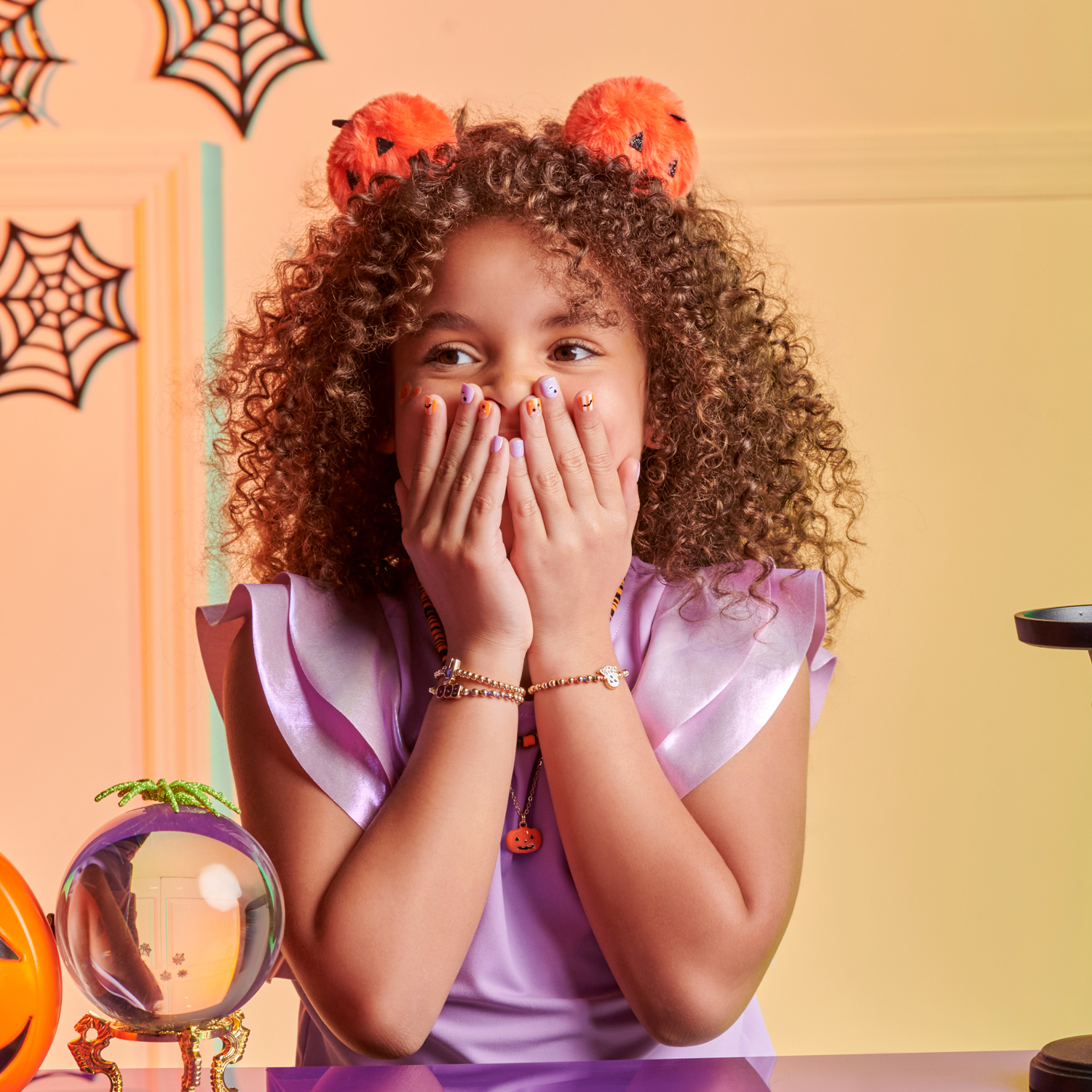 Child wearing Halloween-themed headband with pumpkin design, sitting at a table with decorative items.