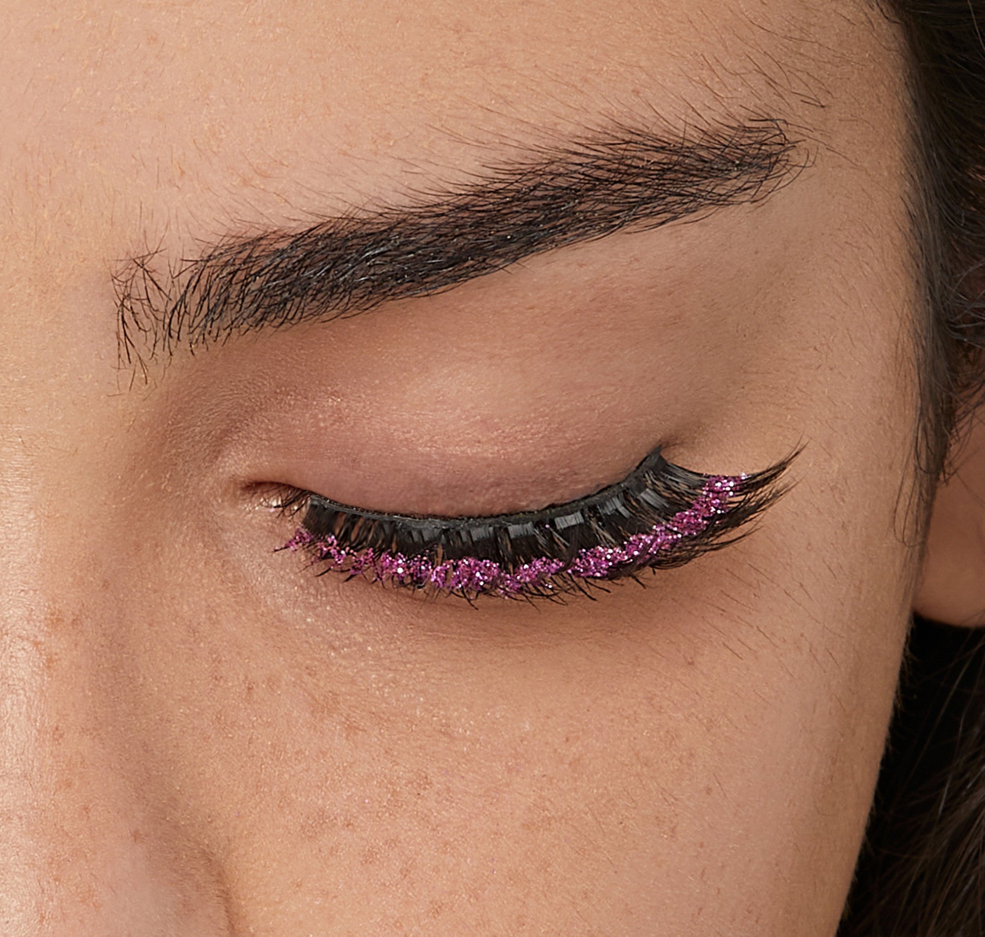 Close-up of eye with black eyeliner, dark lashes, and purple glitter eyeshadow.